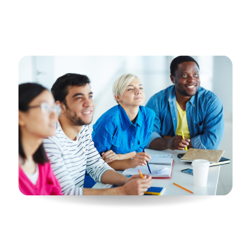 Four people are sitting around a table, pens in hand, smiling.