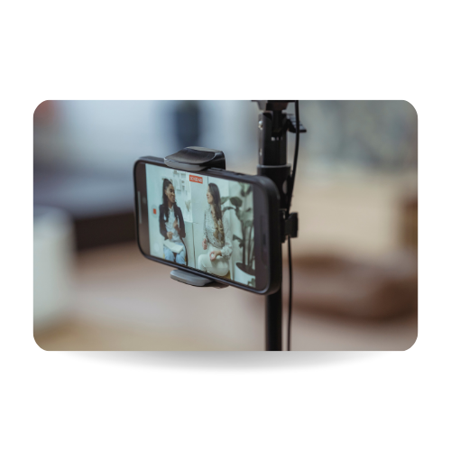 There is a mobile phone standing in a tripod recording an interview with two people