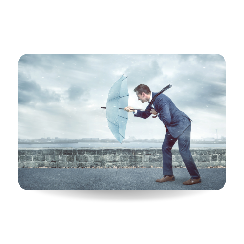 A young business man holding an umbrella to shield himself against a strong headwind. Conceptual image depicting adversity.